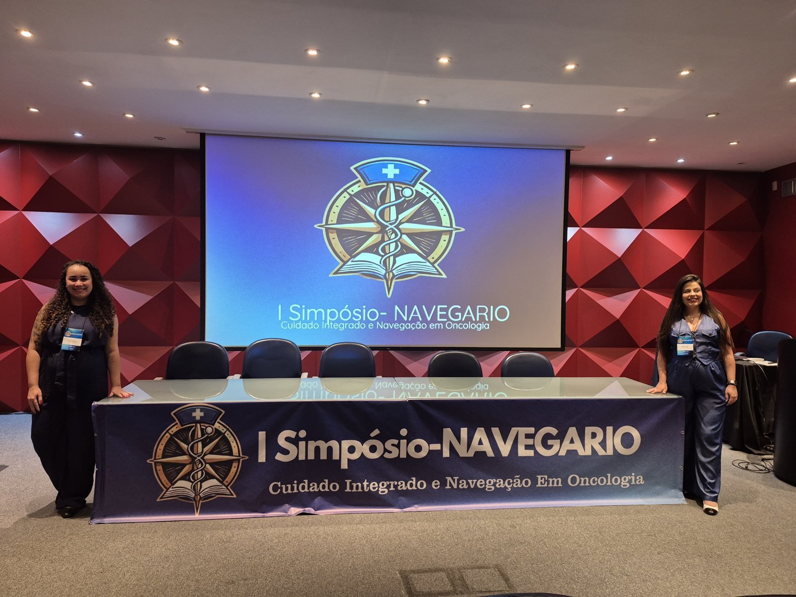 Organizadoras ao lado da mesa com o banner do I Simpósio NavegaRio