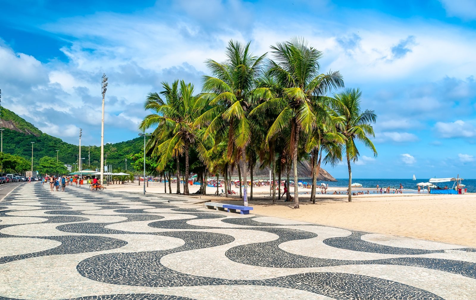 Calçadão de ondas em pedra portuguesa à beira-mar, com coqueiros